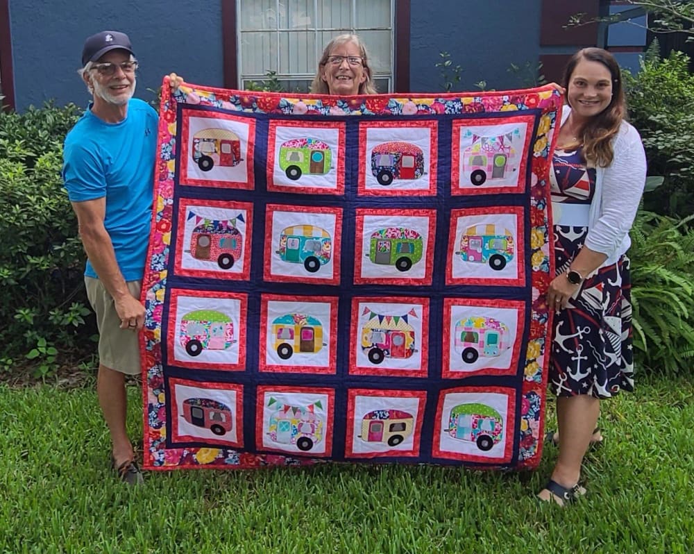 Jaime and two customers holding a finished camper-pattern quilt